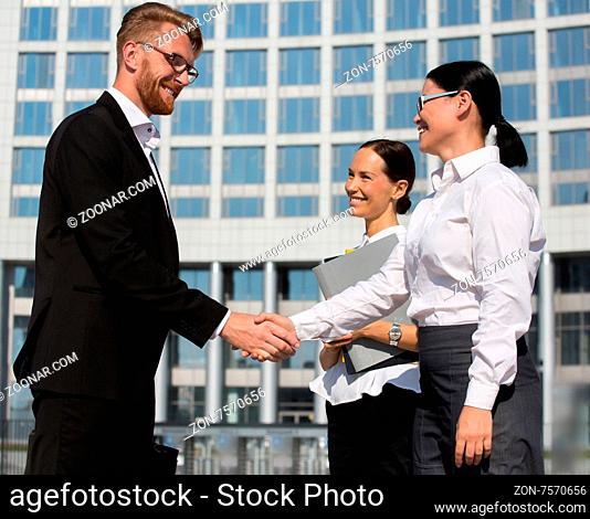 Businesspeople shaking hands. Two confident persons shaking hands and smiling, thecollegue keeping all documents near them