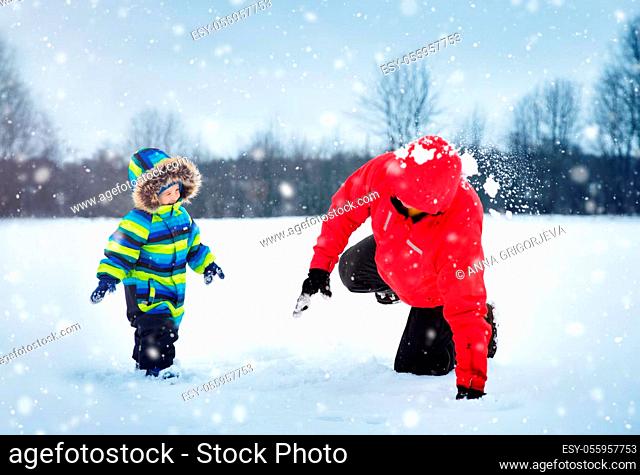 Father with sons walking at snowfall. Children in winter clothes playing with snow and sledding with dad