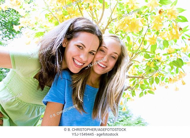 Young mother and teenaged daughter smiling happily under a flowering tree