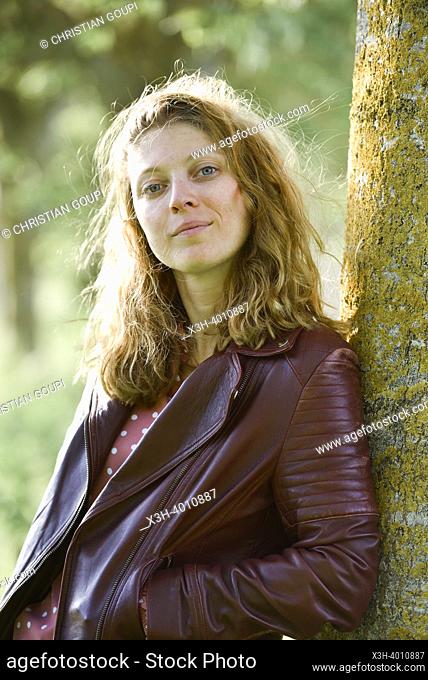 Jeune femme portant un blouson de cuir, adossee au tronc d'un arbre. Departement d'Eure-et-Loir, region Centre-Val-de-Loire, France