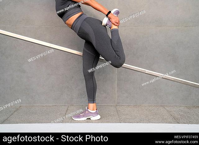 Woman stretching leg on footpath by gray wall