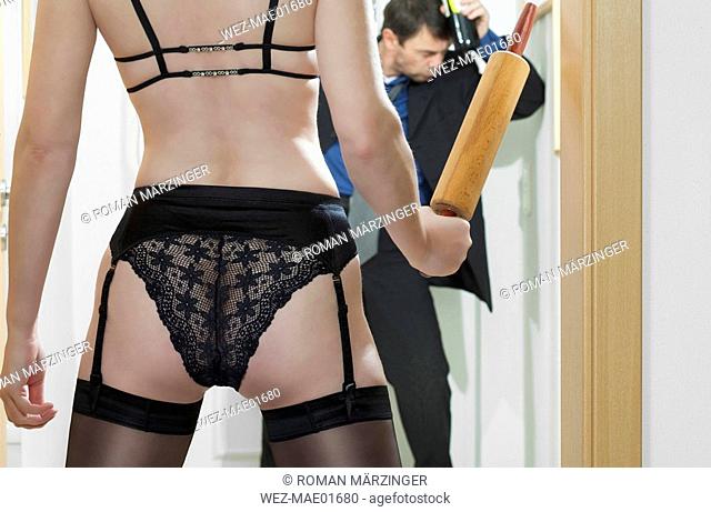 Man coming home, woman waiting with rolling pin, rear view
