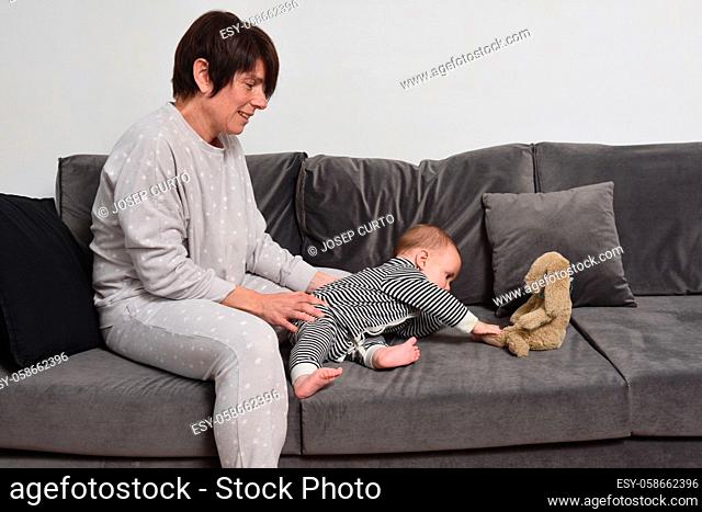 baby with her mother sitting on the sofa the baby wants to take the doll