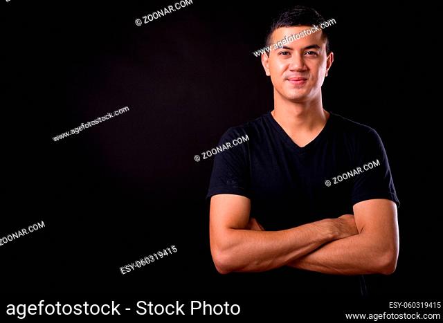 Studio shot of young handsome Asian man against black background