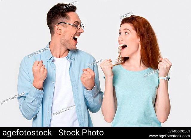 Overjoyed happy attractive young family couple looking at each other, screaming, celebrating success, goal achievement. Winners spouse motivated by unexpected...