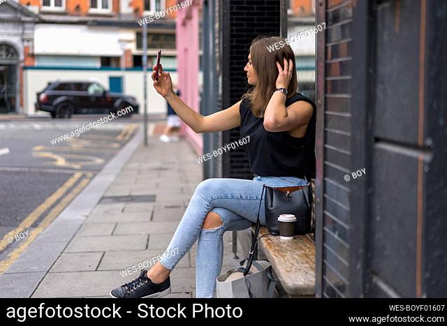 Young woman with hands in hair taking selfie on smart phone