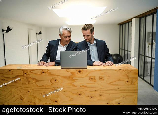 Two businesmen working at counter, looking at laptop, smiling