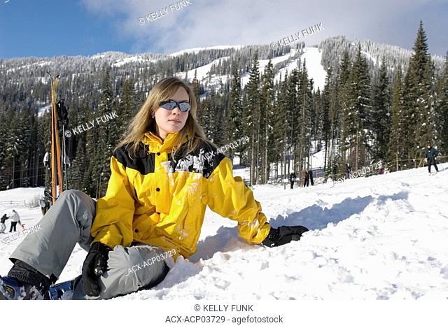 A young women resting at the bottom of a run at Sun Peaks Ski Resort just North of Kamloops, British Columbia, Canada