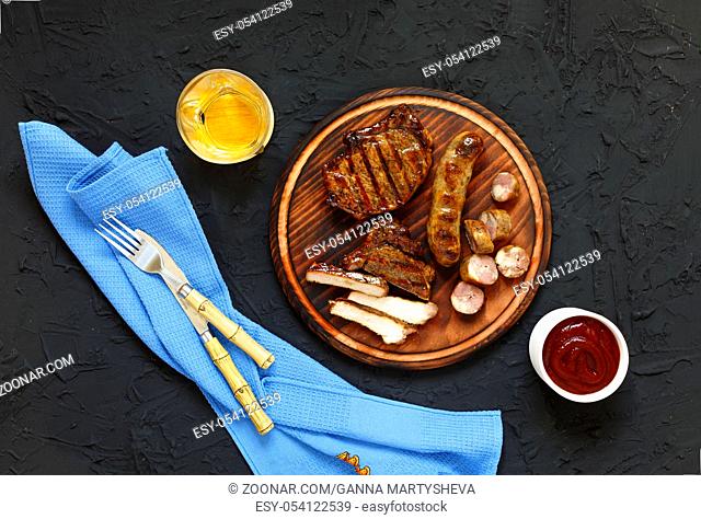 Juicy barbecue steak with ketchup and white wine on a wooden plateau. Stone black background