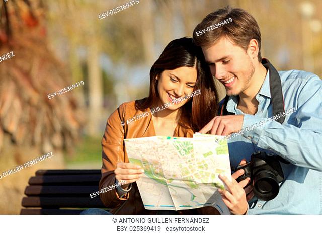 Happy tourists searching landmarks in a map sitting on a bench outdoors