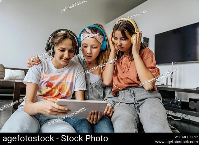 Teenage friends listening music through headphones while using digital tablet at home
