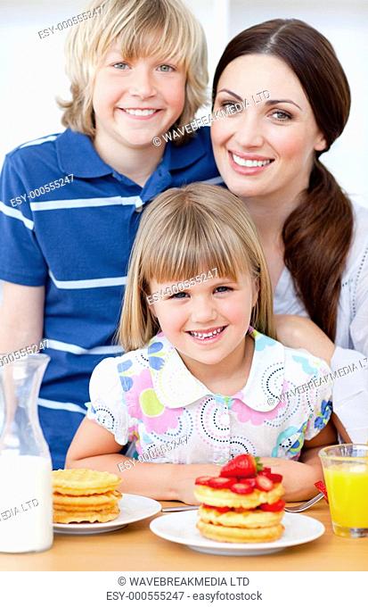 Cheerful mother and her children eating waffles with strawberries in the kitchen