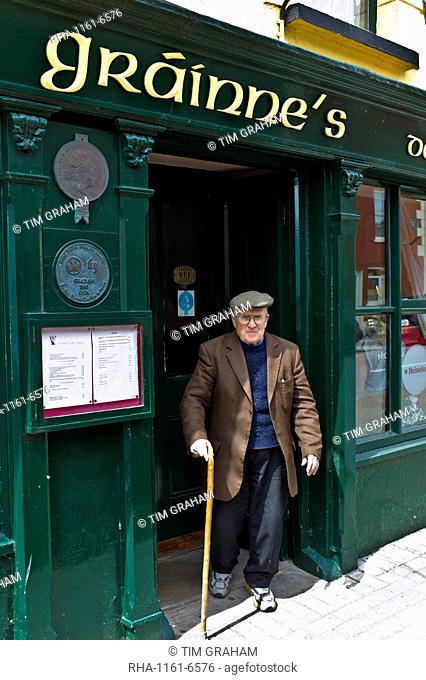 Elderly local Irishman with walking stick leaving Grainne's Bar in Mill Street, Timoleague, West Cork, Ireland