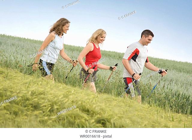 Side profile of two women and man walking with hiking poles in field