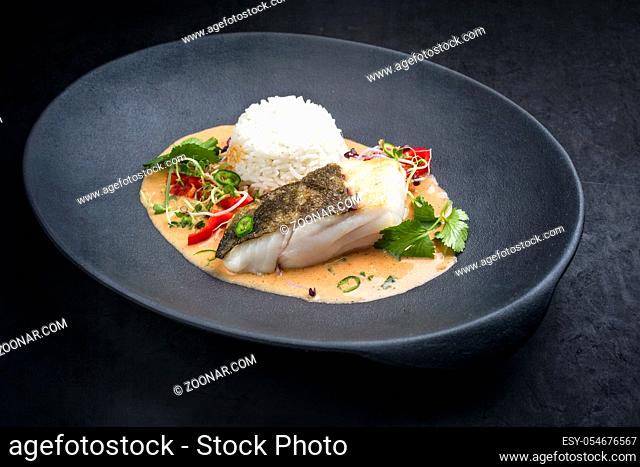Gourmet fried skrei cod fish Thai curry with jasmine rice and chili as closeup on a modern design plate with copy space