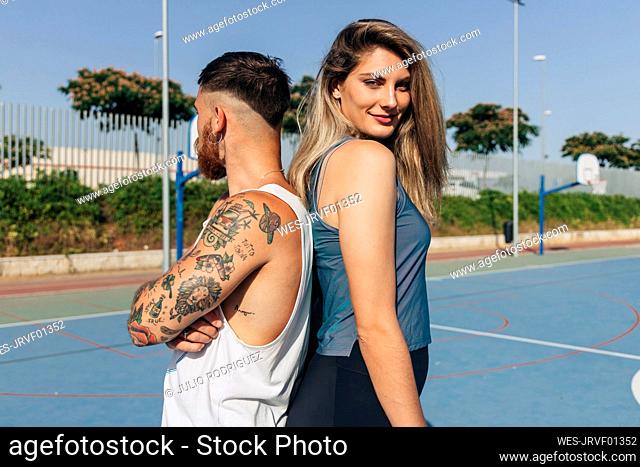 Smiling young woman standing back to back with boyfriend on sunny day