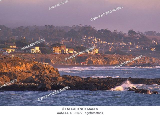 Coastal fog at sunset over quaint small town village atop rocky bluffs over the Pacific Ocean, Cambria, California