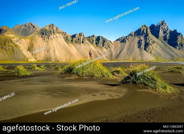 Iceland. Aerial view of woman hiker with backpack at black sand dunes on the Stokksnes headland on southeastern Icelandic coast with Vestrahorn