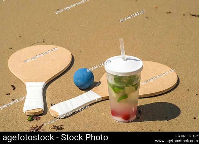 Beach tennis rackets in sand, caipirinha drink