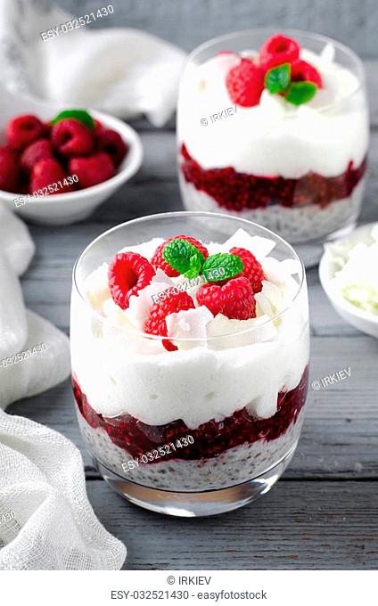 Healthy breakfast, desert, with chia seed pudding, cream, raspberry jam, coconut flakes and fresh berries, on wooden background