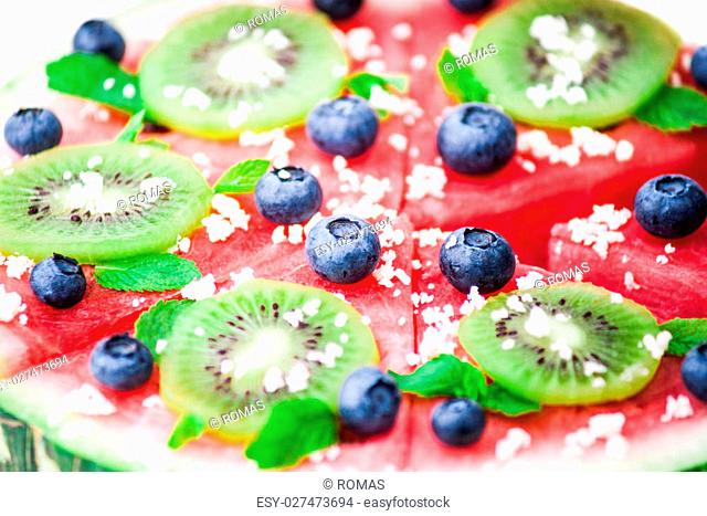 Sliced juicy watermelon pizza isolated on white, closeup view from above. Ingredients are watermelon, blueberries, kiwi, mint, and coconut shavings