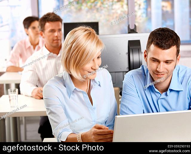 Young business people sitting at desk, using computer at business training, smiling