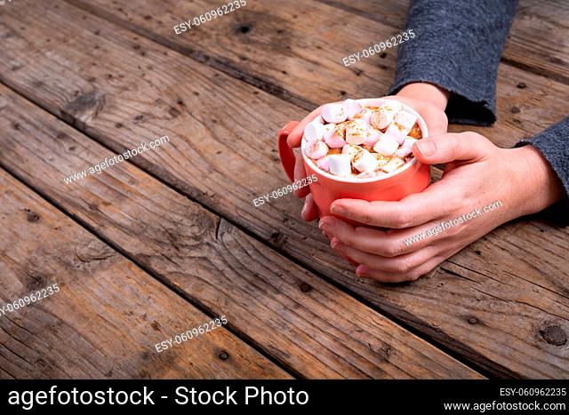 Cropped hands of woman holding mug of hot chocolate drink and marshmallows at table with copy space