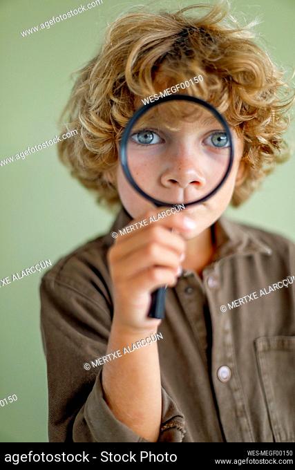 Boy looking through magnifying glass against green background