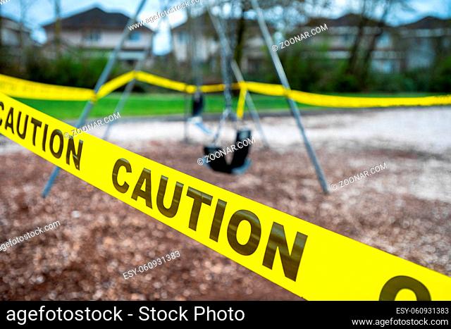 Black rubber swings on chains in closed public playground surrounded by yellow caution tape during time of Corvid-19 Coronavirus pandemic
