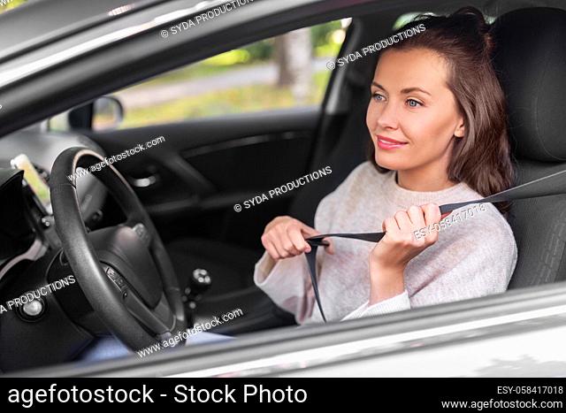 woman or female car driver fastening seat belt