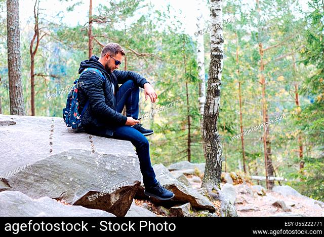 guy sits in the woods on a rock and makes a selfie