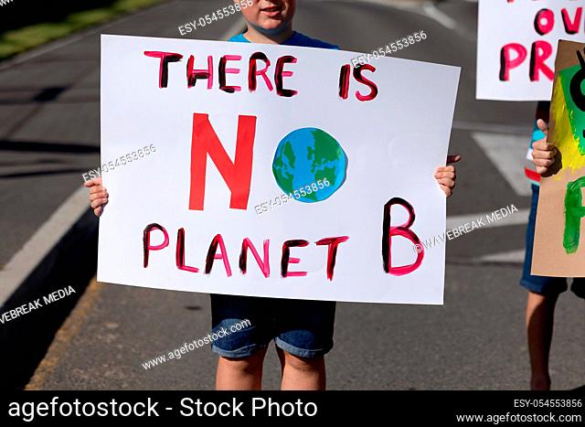 Front view mid section of a Caucasian elementary school boy on a protest march, carrying a sign with environmental conservation slogan on it