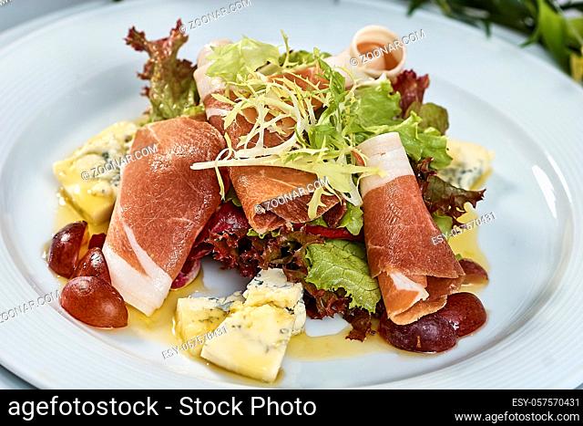 meat salad with ham cheese lettuce Dorblu grapes and olive oil served on a plate on a table with flowers