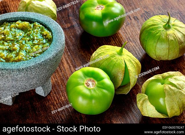 Tomatillos, green tomatoes, with salsa verde, green sauce, in a molcajete, traditional Mexican mortar, on a dark rustic wooden background