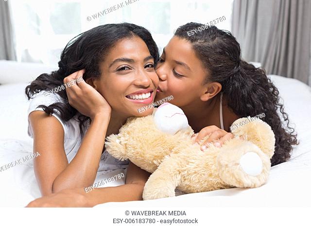Pretty woman lying on bed with her daughter kissing cheek