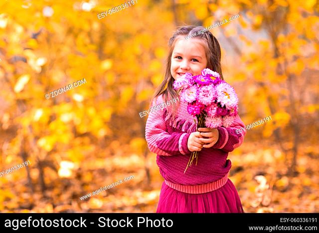 Cute little girl standing in autumn park with pink flower bouquet