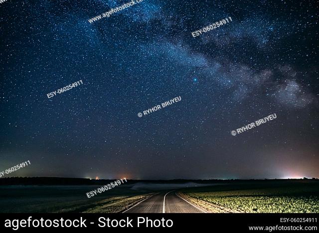 Blue Night Starry Sky Above Country Asphalt Road In Countryside And Green Field. Night View Of Natural Glowing Stars And Milky Way Galaxy