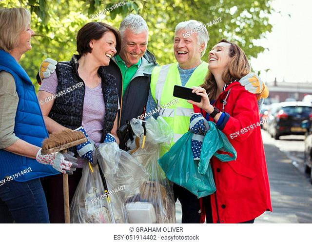 A group of five people who are participating in a city clean-up laughing together
