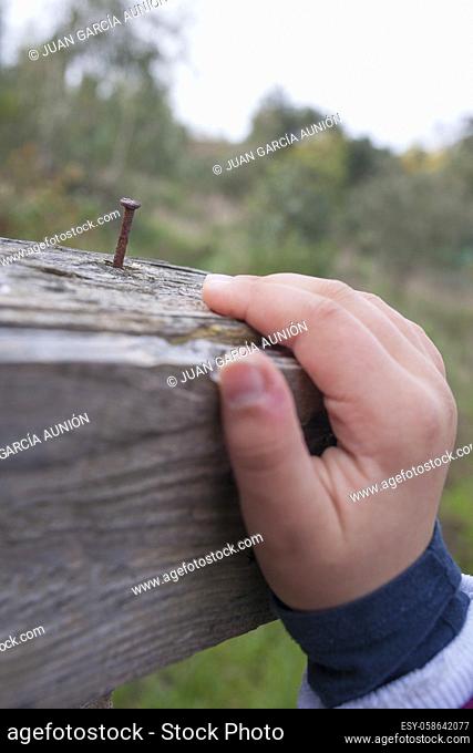 Child boy hand grabbing a board with rusty nail near. Selective focus