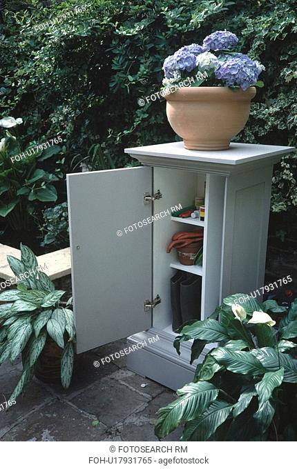Hydrangea in terracotta pot on small outdoor storage cupboard with door open
