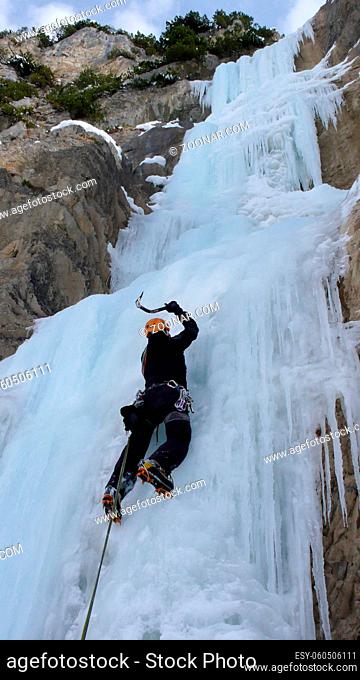 male ice climber on a steep frozen waterfall on a beautiful winter day in the mountains of Liechtenstein