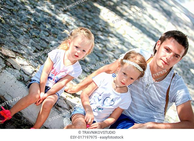 Young father with little daughters sitting on street in old greek town