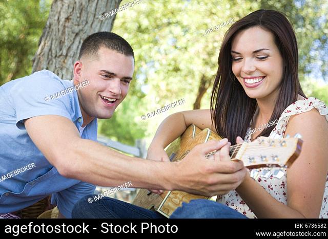 Handsome young man teaching mixed-race girl to play guitar at the park