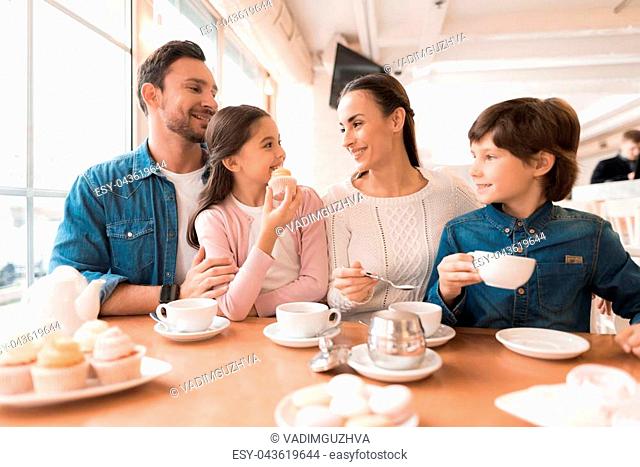 A young family came together in a cafe. Mom, dad, little daughter and son drink tea, eat cakes. They are happy together