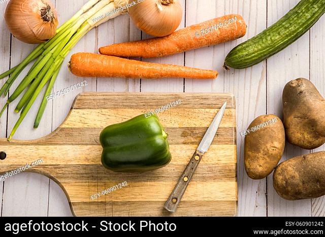 An assortment of vegetables such as onions, carrots, potatoes, and green bell pepper and a cutting board