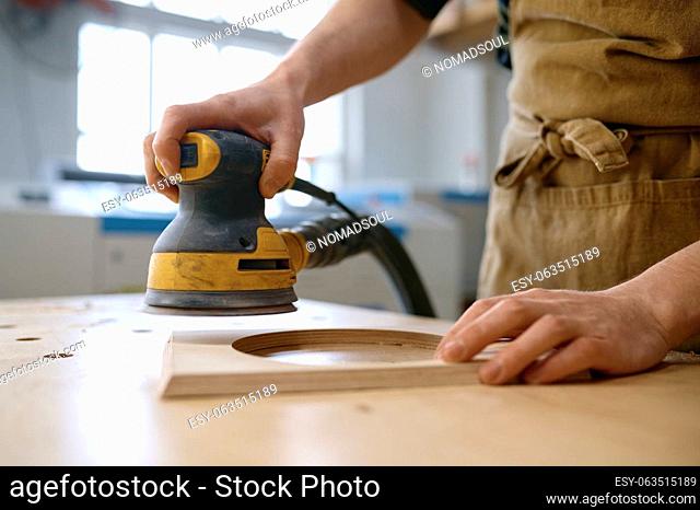Closeup craftsman hands working with eccentric grinding machine at carpentry workshop. Orbital sanding process