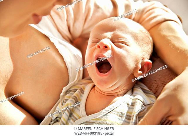 Mother holding her yawning newborn baby