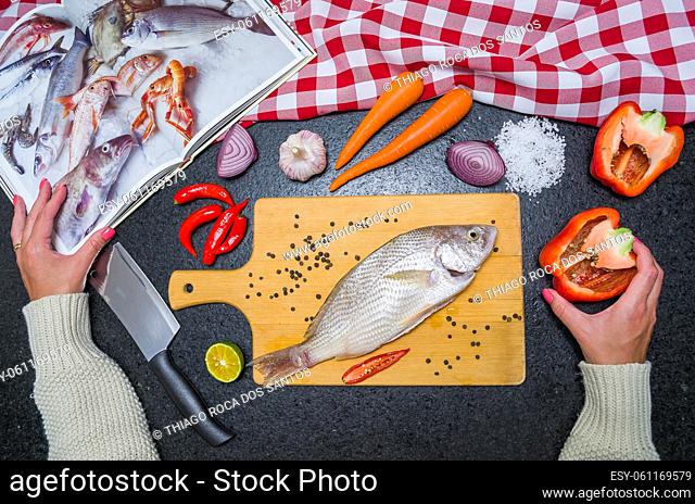 Preparing a gastronomic dish of roasted corvina, Young woman consulted the cookbook while preparing the recipe