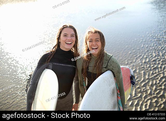 Portrait happy young female surfers with surfboards on wet beach