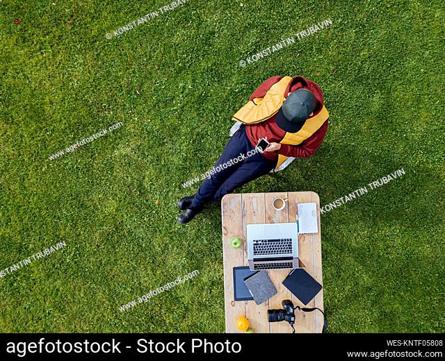 Aerial view of man using smart phone at coffee table set on green lawn